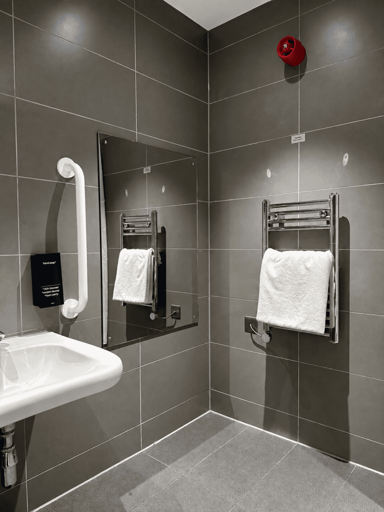 Accessible bathroom at Staycity Manchester Piccadilly with toilet support rails, lowered sink and mirror.