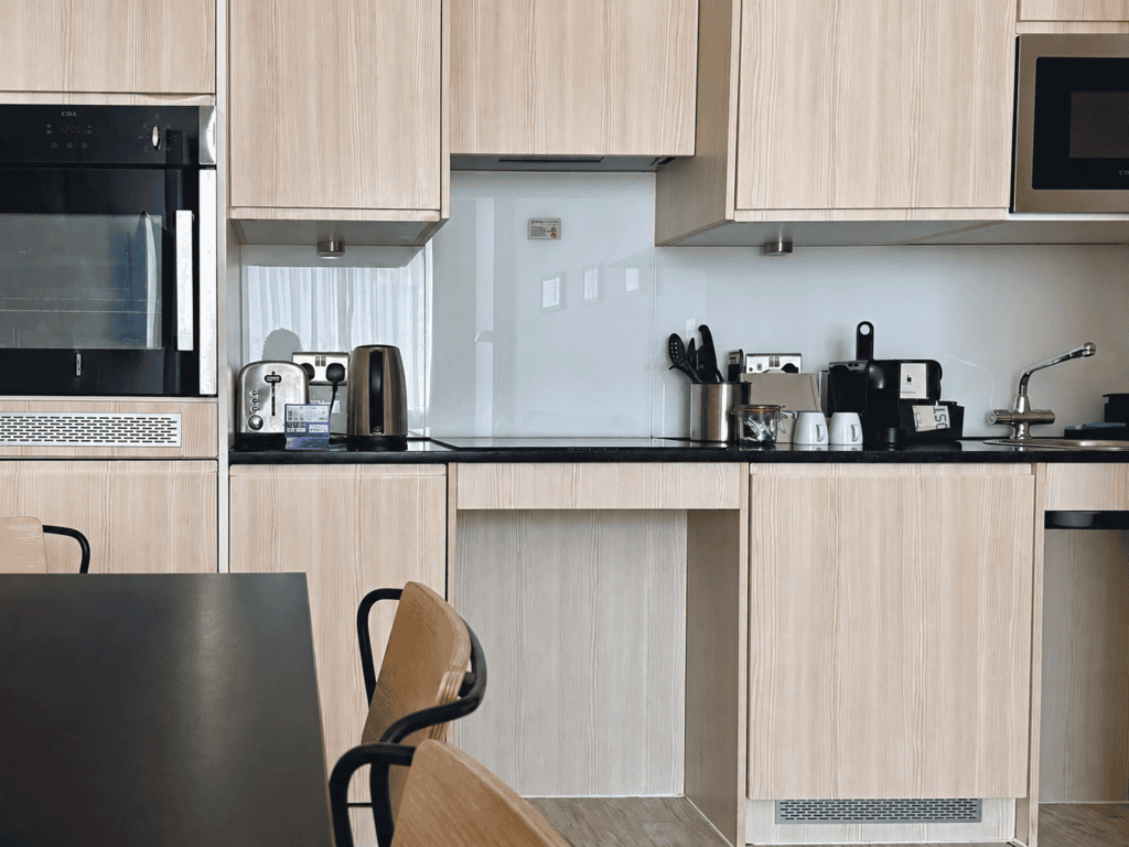 Kitchen at Staycity Manchester Piccadilly with light wood units, worktops, sink and appliances beside the dining area.