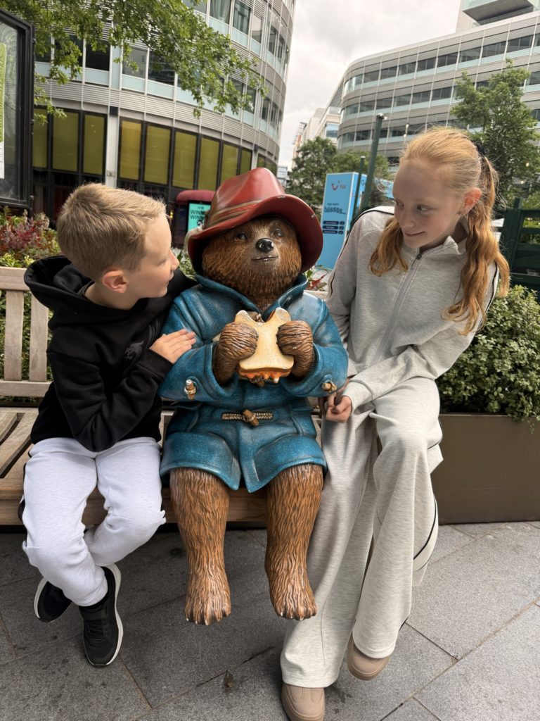 Two childre sitting on a bench with Paddington Bear statue Race Across the World Experience | Manchester | Wheelchair accessible route