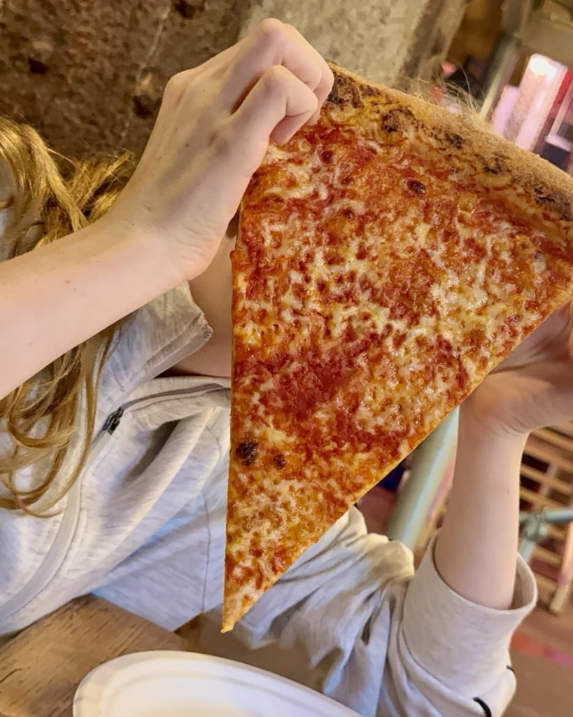 Child holding up a slice of pizza in fron t of her face Nell's Slics | Freight Island | Manchester | Accessible Restaurant
