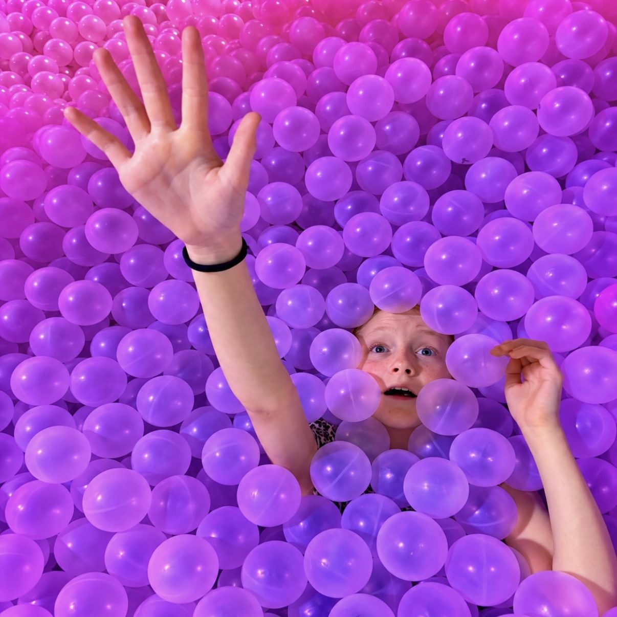 girl reaching arm out of a ball pool at Bubble Planet Manchester during an accessible family city break.