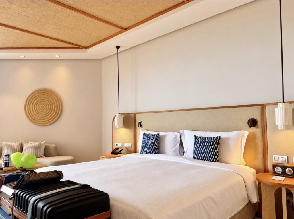 Guest bedroom at The Ritz-Carlton Abama, with white bedding, navy patterned cushions, natural wood furnishings and luggage in the foreground.